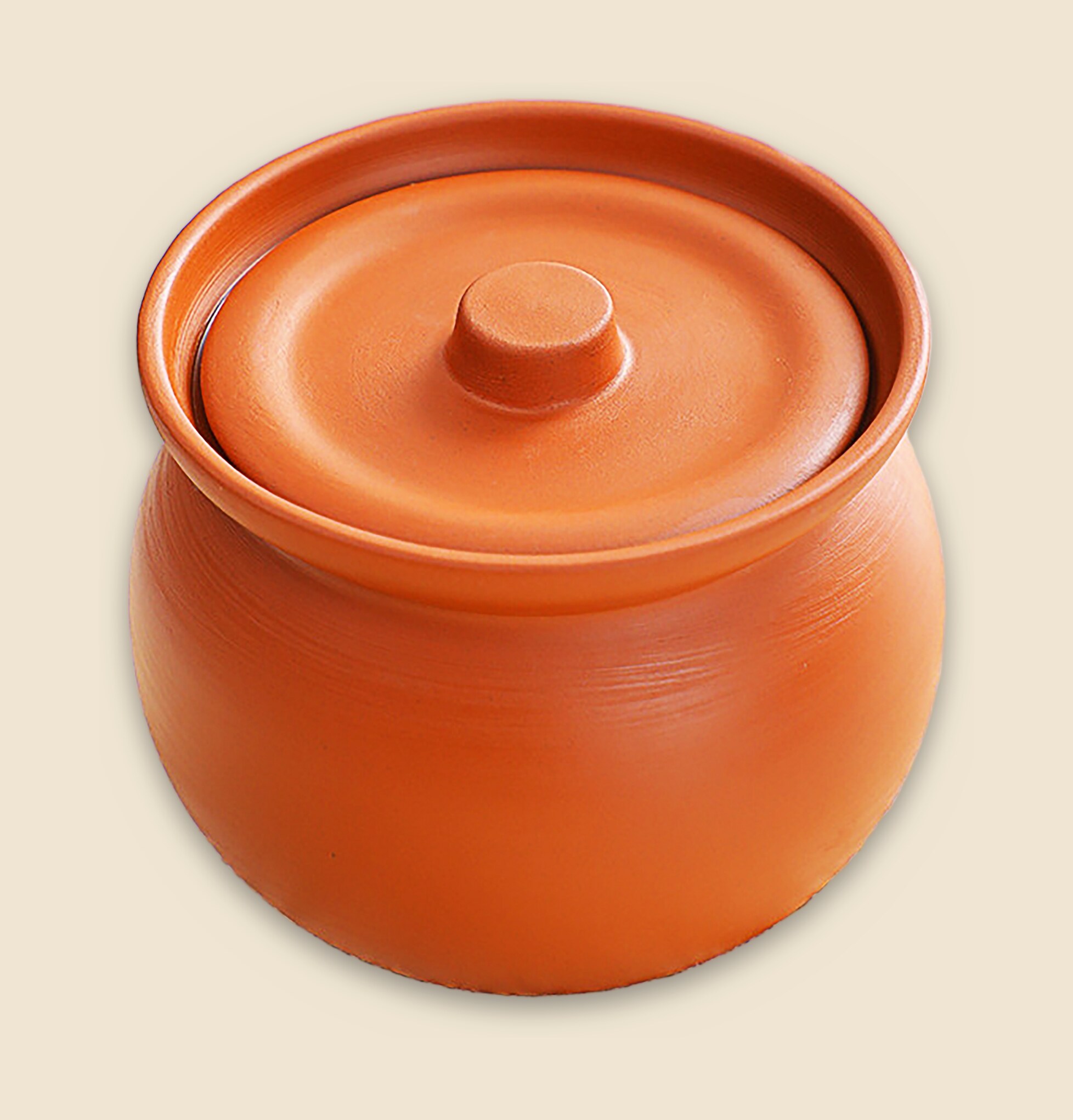 A handcrafted terracotta clay pot with lid on a warm cream background